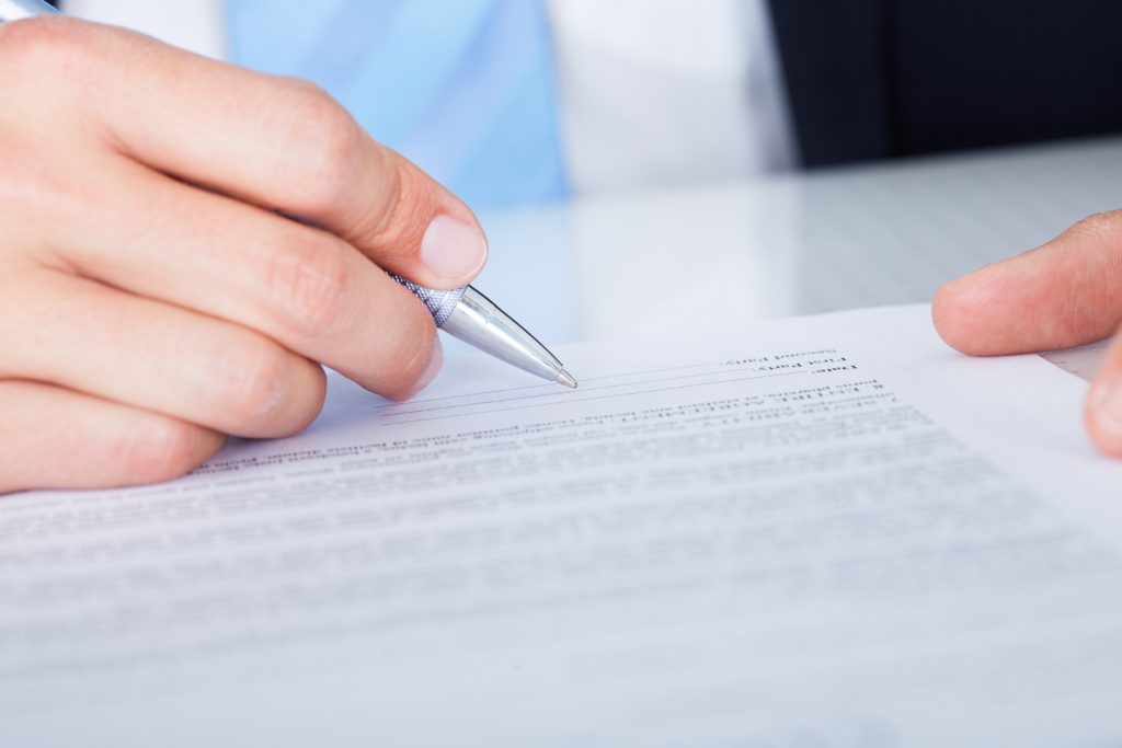 Close-up Of Businessman Signing Contract Paper With Pen
