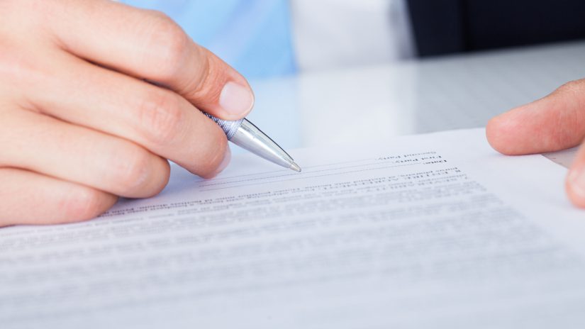 Close-up Of Businessman Signing Contract Paper With Pen