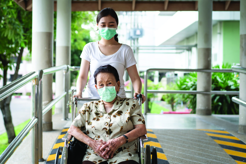 A senior in a wheelchair being assisted by a young woman.