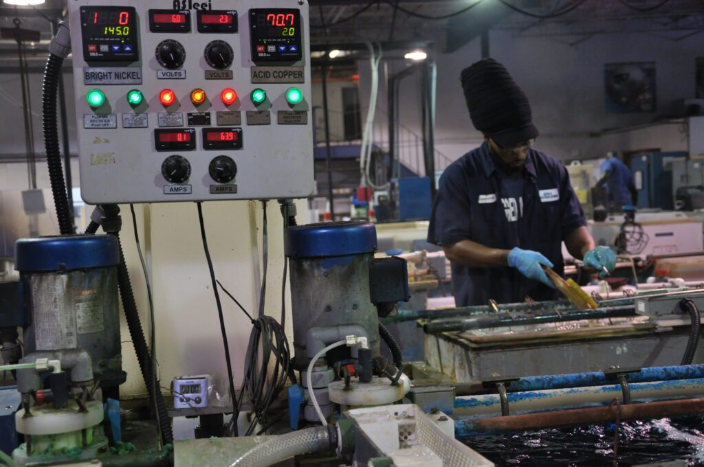 a man wearing gloves works on electroplating equipment