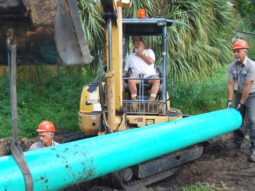 Pinellas County utilities staff install a pipe using a backhoe.
