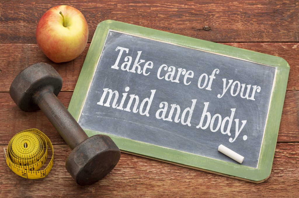 Take care of your mind and body -  slate blackboard sign against weathered red painted barn wood with a dumbbell, apple and tape measure