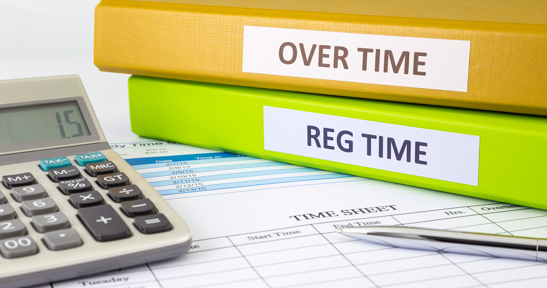 Binders with overtime and reg time printed on the spines on a desk with a calculator and timesheet