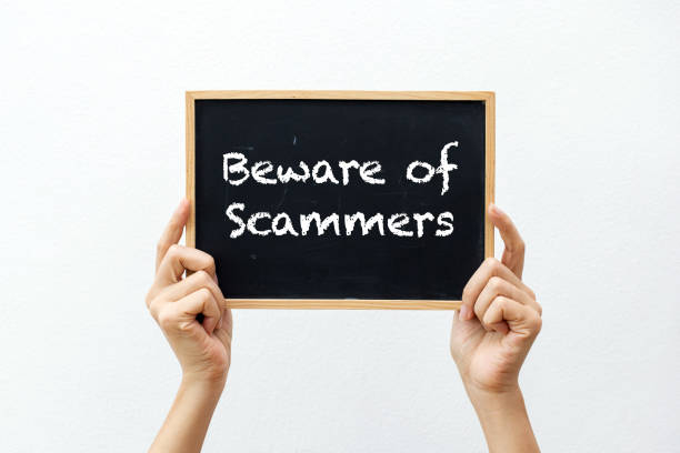 Cropped hands holding a chalkboard with "Beware of Scammers" against a white background