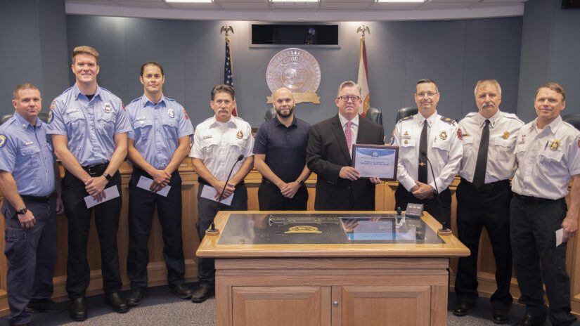 Photograph of Chairman Justice holding a plaque with seven Pinellas County fire professionals in the Assembly Room
