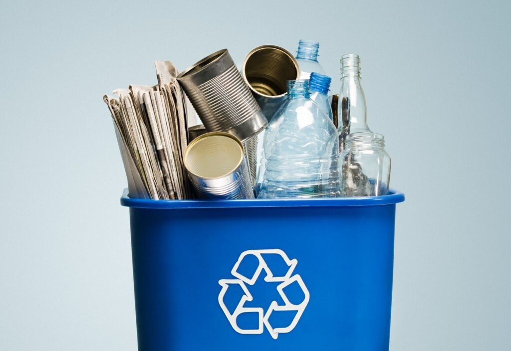 Image of a blue recycling bin containing newspaper, tin cans, plastic bottles and glass bottles & jugs