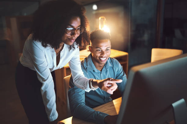 Shot of two businesspeople working together on a computer in an office at night