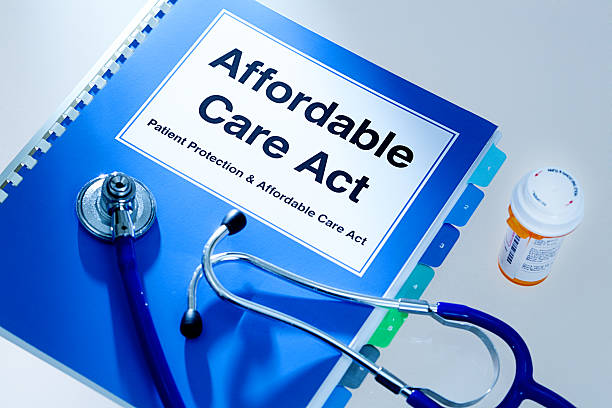 Still life of a manual handbook for the Patient Protection and Affordable Care Act with a stethoscope and prescription medication bottle. The manual is open to the title page, The open enrollment of the Affordable Care Act of the United States offers a health insurance program for all the U.S. citizens across the country.