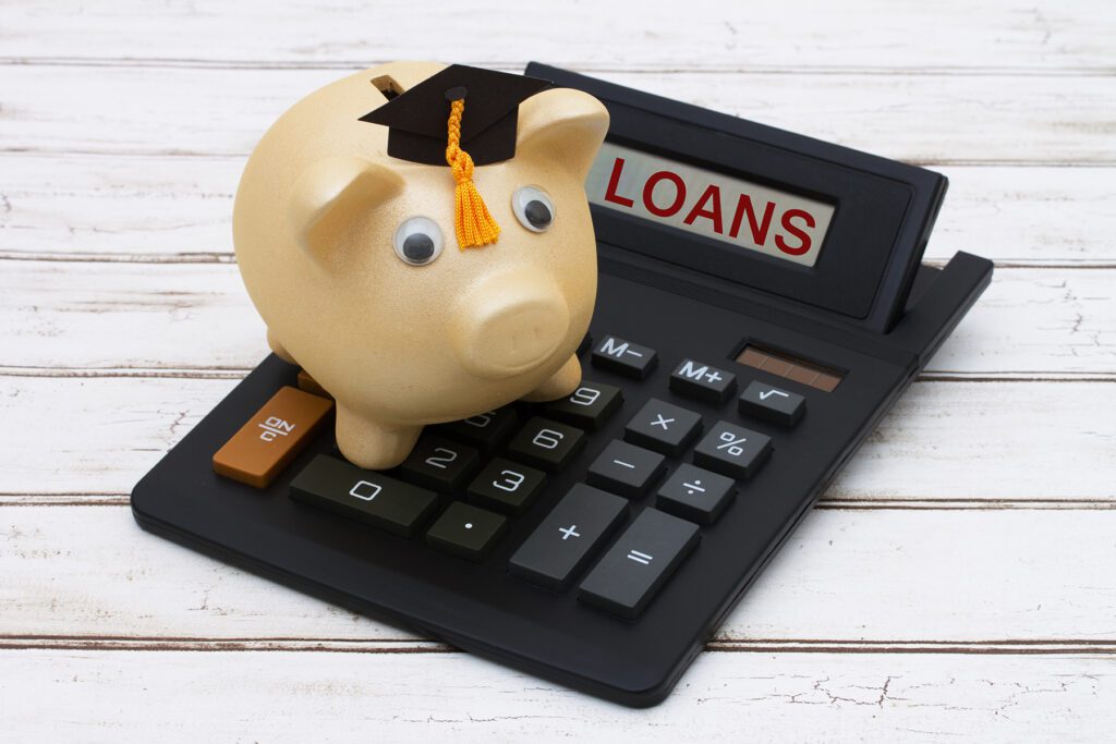 Calculating your student loans, A golden piggy bank with a grad hat on a calculator with word loans over a distressed wood background