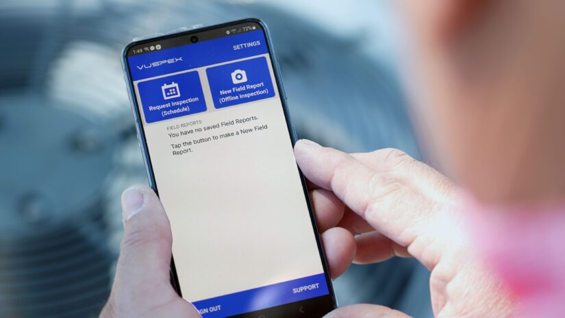 A man holds a cell phone showing the VuSpex, virtual inspections application.