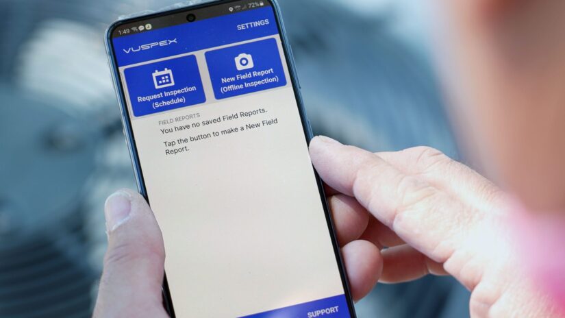 A man holds a cell phone showing the VuSpex, virtual inspections application.