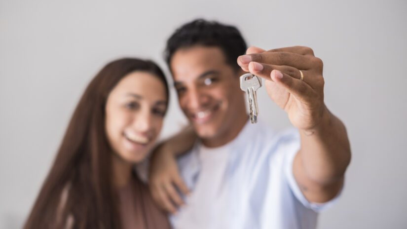 Close up of new home keys and young interracial couple smile and show the property - new life mortage house buyers people concept - happy youth family in love and relationship showing key