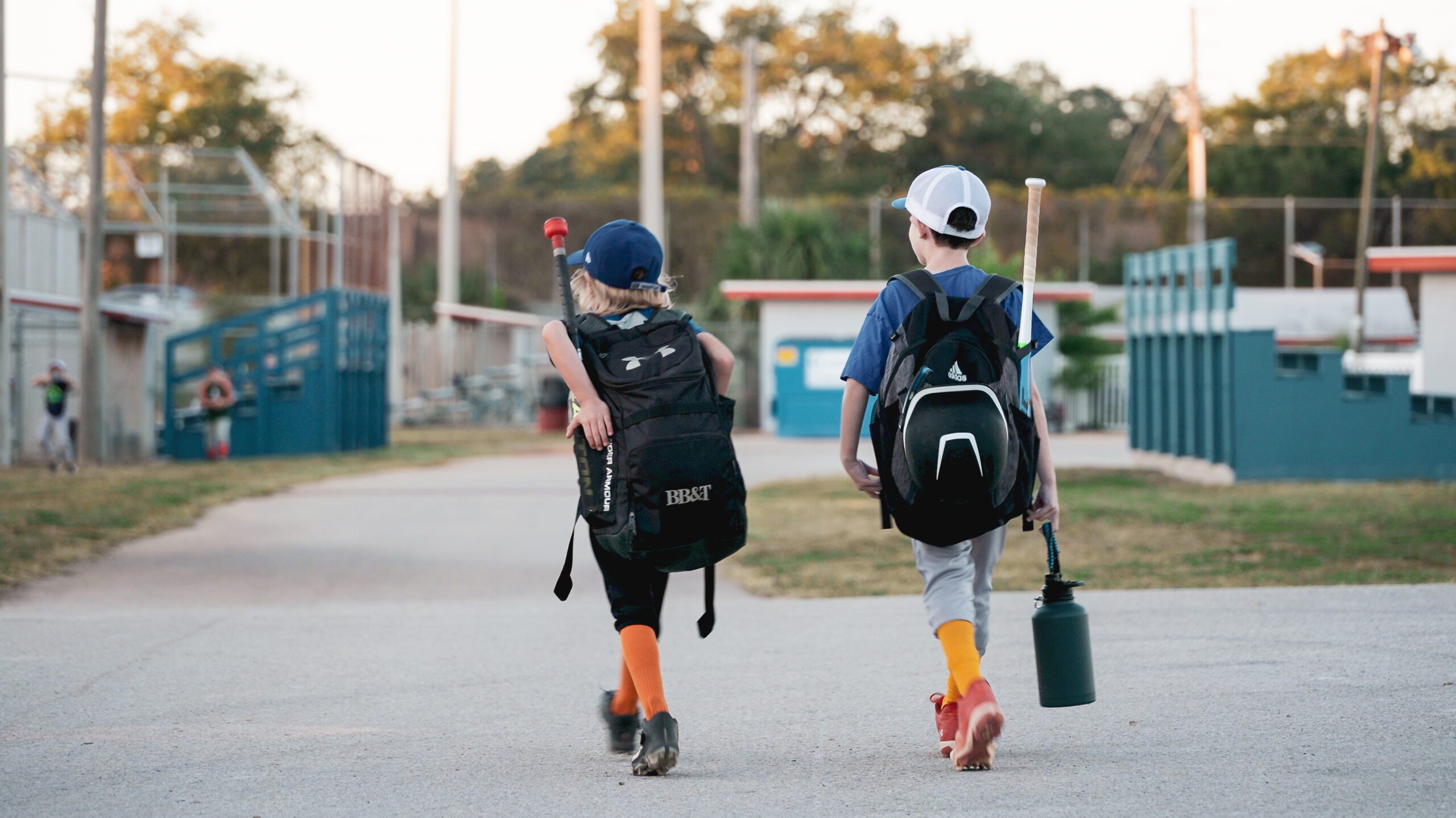 Two young baseball players walking away from the camera toward the field.