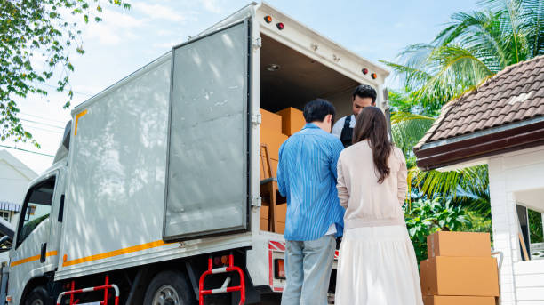 Asian Couple check while unloading boxes and furniture from a pickup truck to a new house with service cargo two men movers worker in uniform lifting boxes. concept of Home moving and delivery.