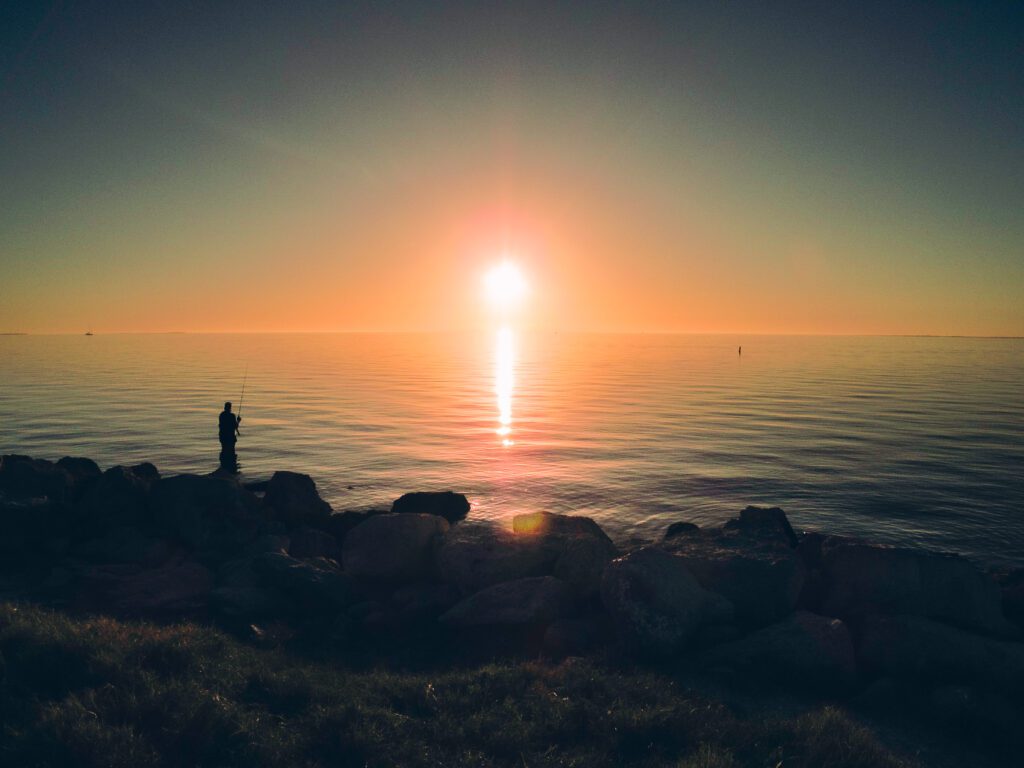 Photo of a person fishing along rocky shore at sunset