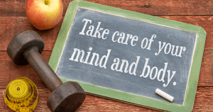 Take care of your mind and body - slate blackboard sign against weathered red painted barn wood with a dumbbell, apple and tape measure