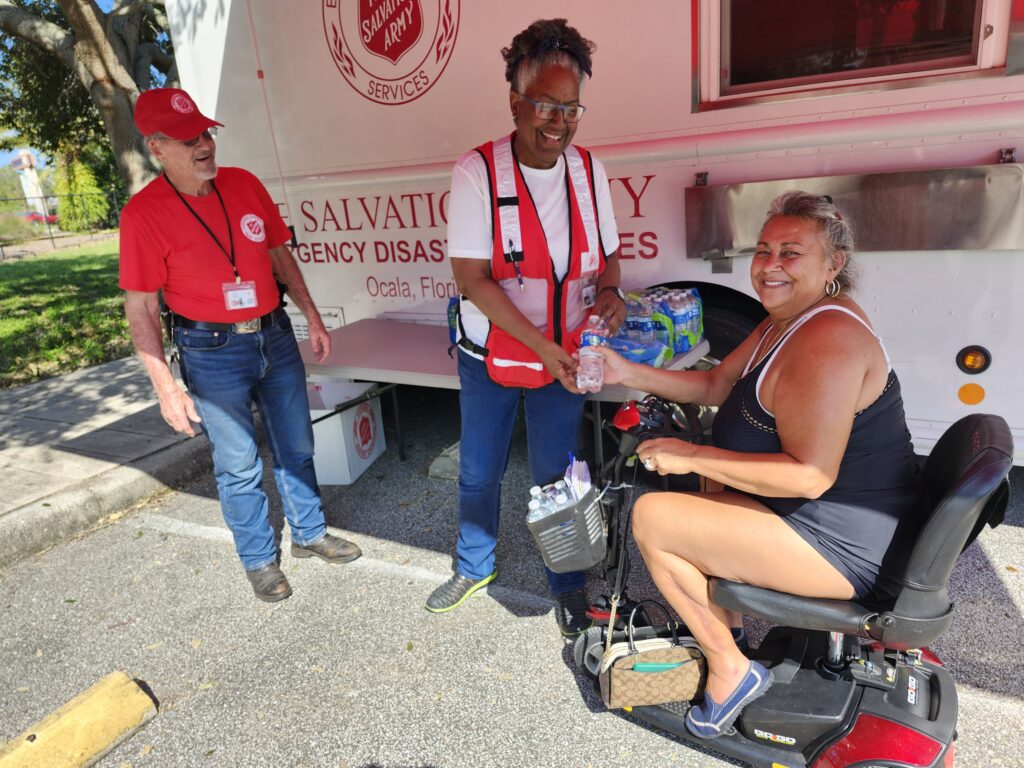 Salvation Army volunteers hand water to a woman in front of the Salvation Army truck.