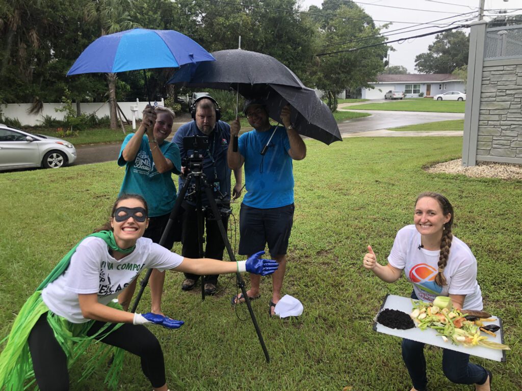 Two people posing with food scraps in front of a camera crew in an outdoor field.