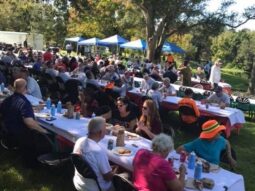 People at picnic tables in a field at an event.