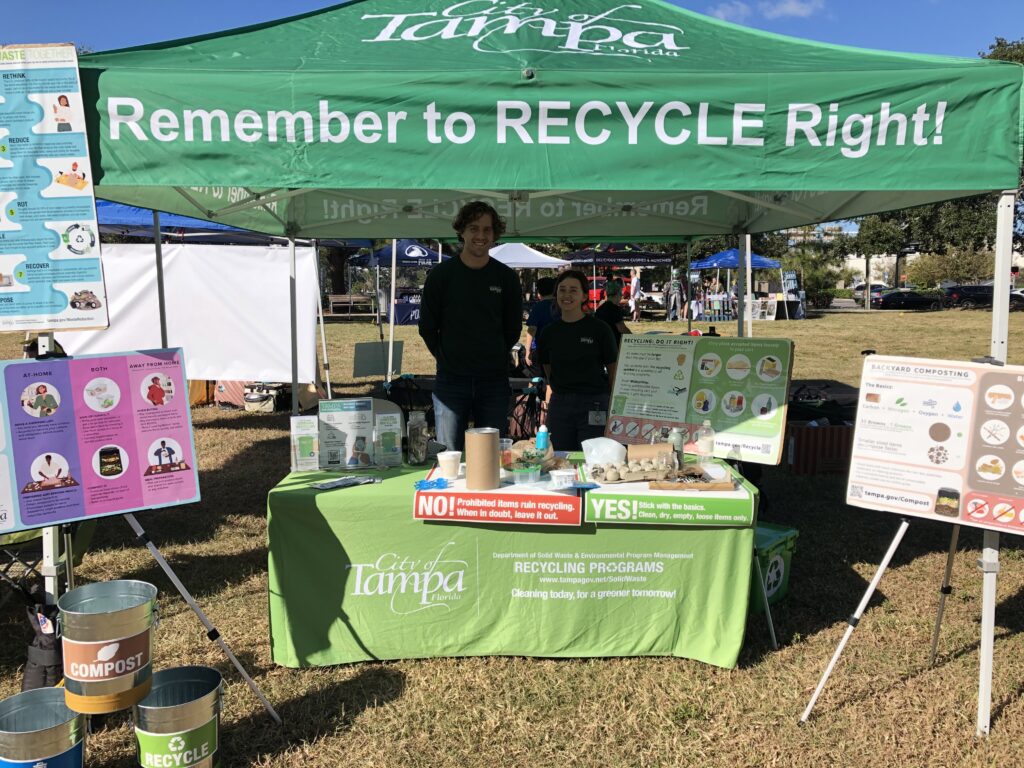 Two people standing under a tent at a vendor table for City of Tampa recycling.