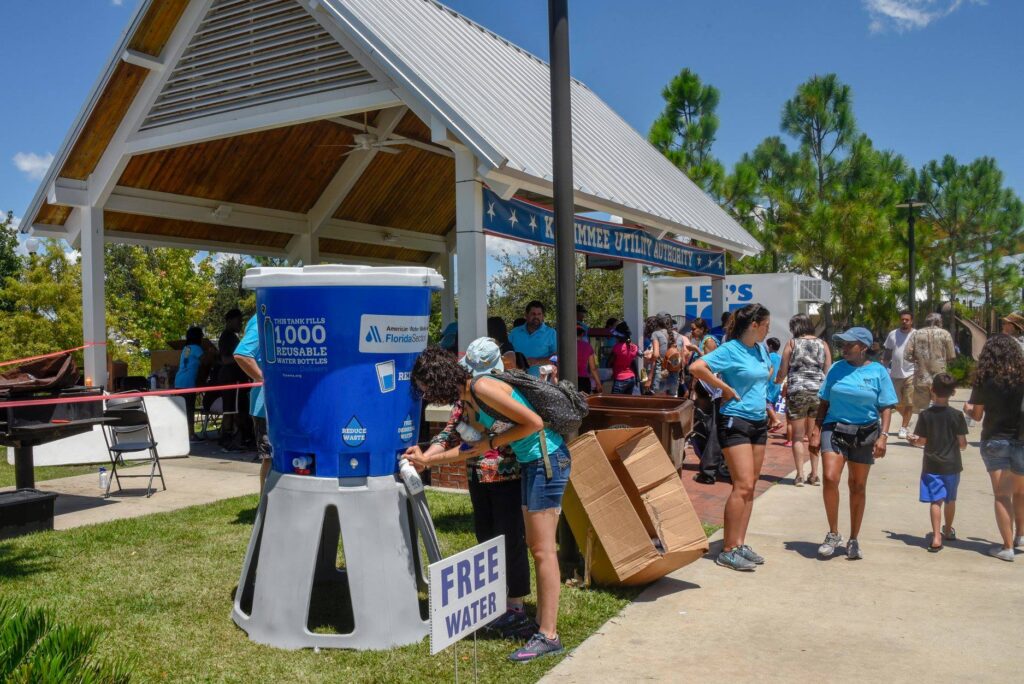 Two people filling up water bottles from a cooler at a summer outdoor event.