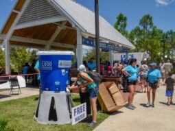 Two people filling up water bottles from a cooler at a summer outdoor event.