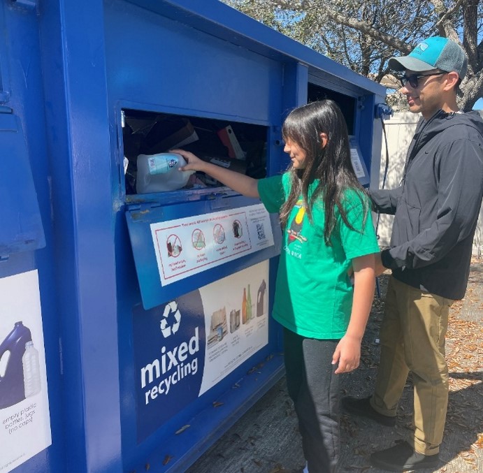 A man and girl placing recyclables into a container at a mixed recycling drop-off center