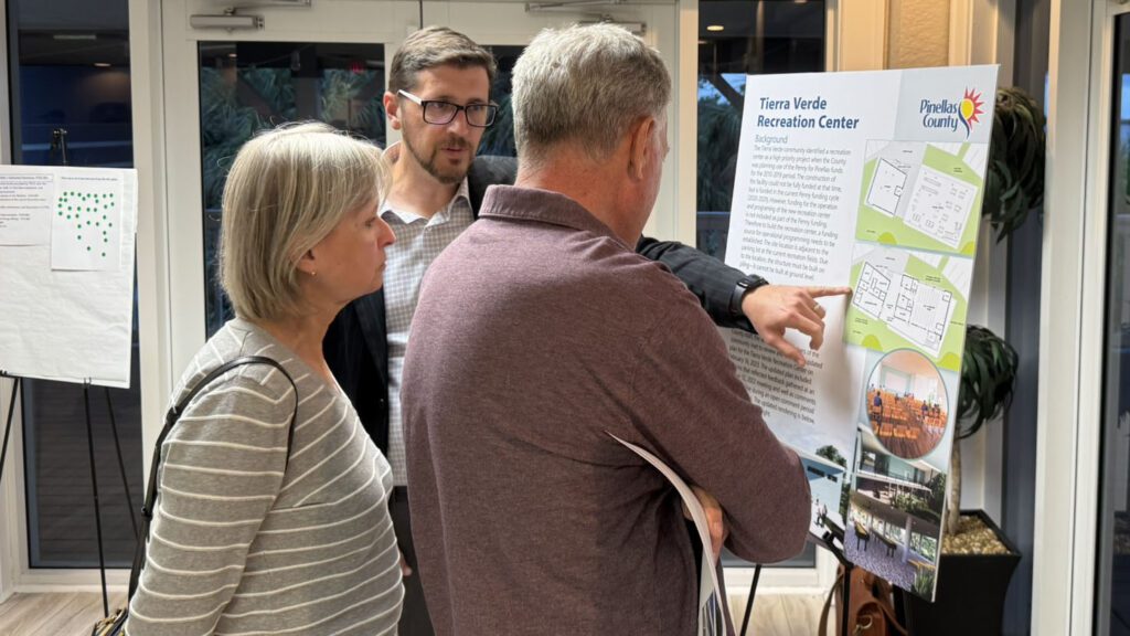 A photograph of a man and woman looking at a poster about the proposed Tierra Verde recreation center, while a male county staff person points at a section of the floor plan.