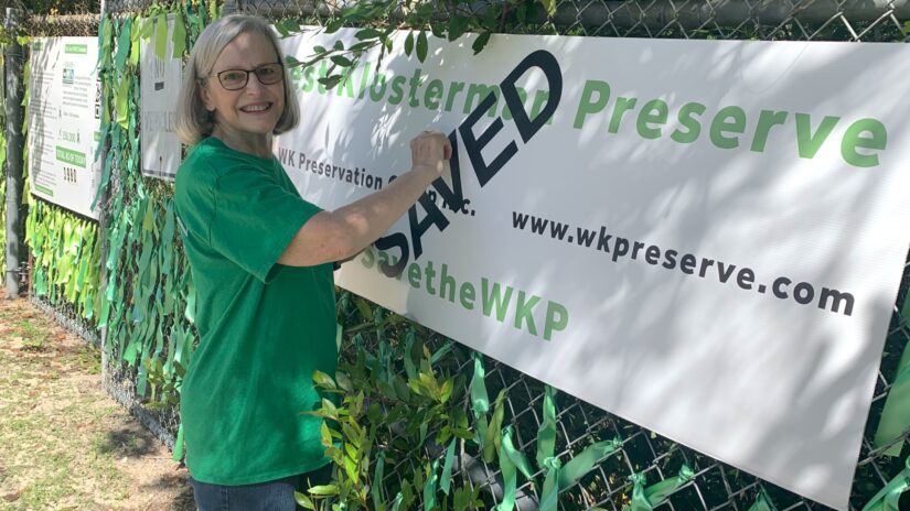 ​A member of the WK Preservation Group stands before a banner declaring the 14-acre West Klosterman Preserve near Tarpon Springs "saved" from development. This conservation success was achieved through a partnership between Pinellas County and the nonprofit group, with each contributing $1.5 million to acquire the land. The purchase was finalized Thursday, April 10, 2025.