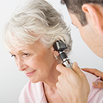 Doctor examining female patient's ear using otoscope in clinic