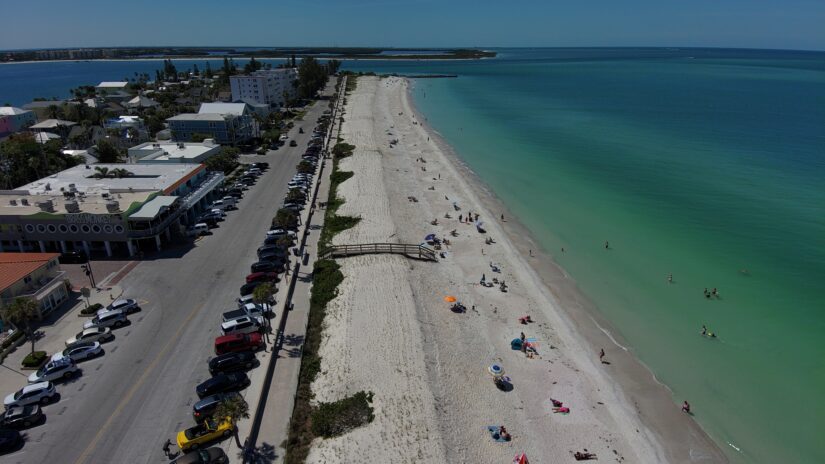 An aerial photograph of Pass-a-Grille Beach looking south, showing newly created dunes and people swimming and enjoying the beach.