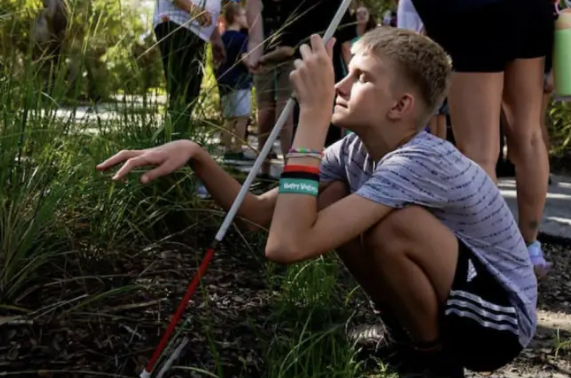 Gabe Wahlberg, 14, crouches down to touch some grass along the path while taking a nature walk with other children with Lighthouse of Pinellas, a resource center for the visually impaired, during an outing at Weedon Island Preserve as part of their summer camp programming to experience being outdoors and connect with nature on Monday in St. Petersburg.