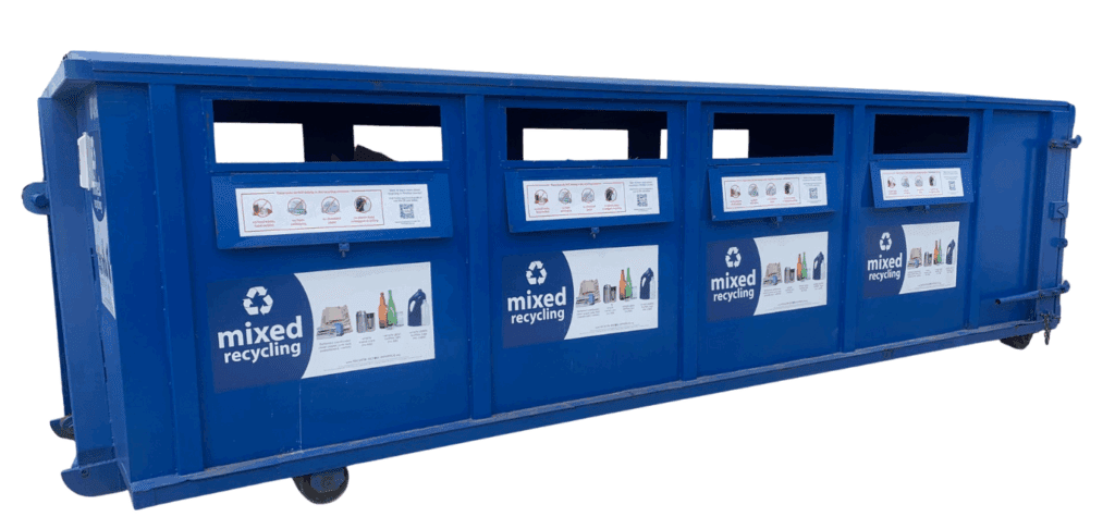 A large blue dumpster with four rectangle openings in a row on the side at the top of the container for placing items. The container has mixed recycling labels for what belongs in the bin.