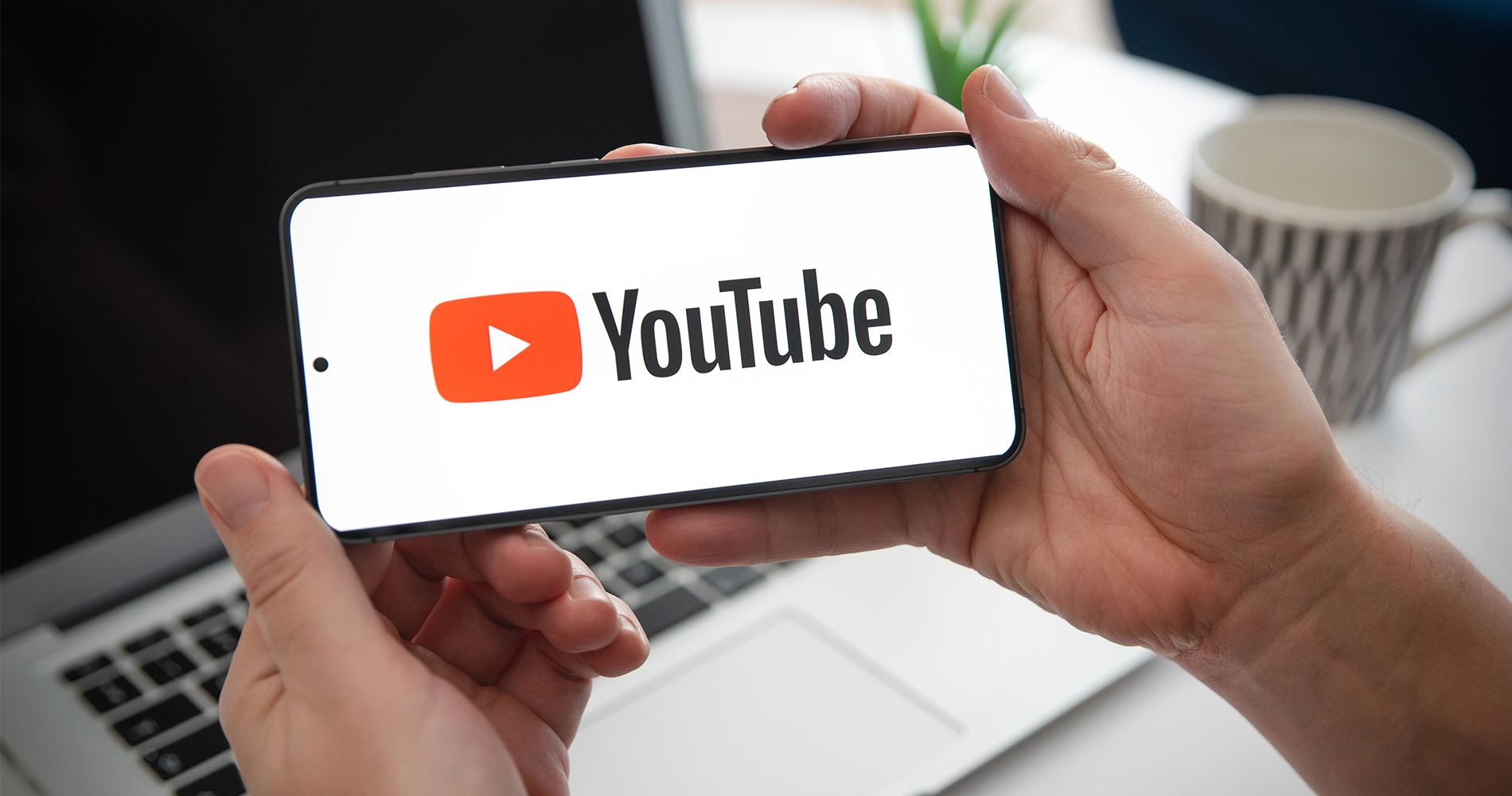 Hands holding a cell phone with the YouTube logo on the screen