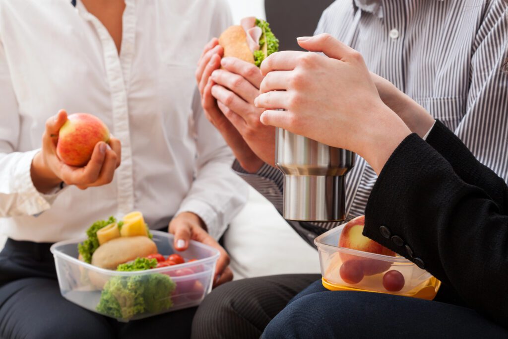 Closeup of employees hands holding coffee cup and lunch items such as fruit and sandwich