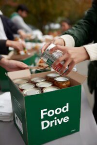 Food drive box with hands placing canned goods inside the box