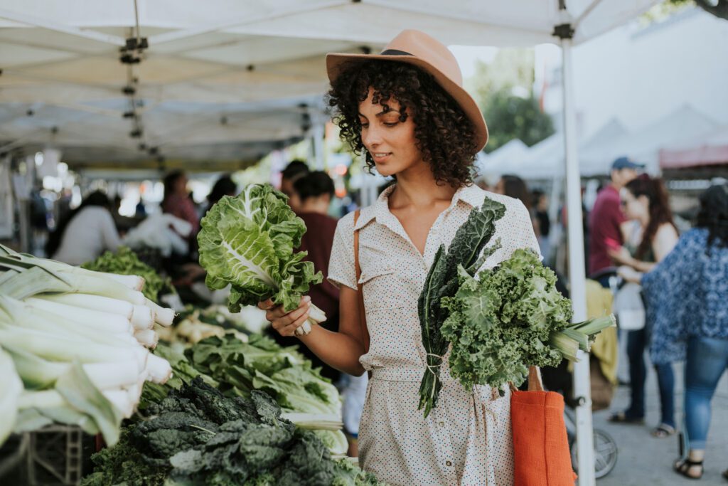 Image of a person shopping for lettuce at a farmers market and using a reusable bag. 