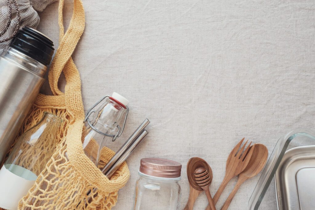 Image of reusable items including water bottle, reusable grocery bag, jars, bamboo cutlery and glass takeout containers. 