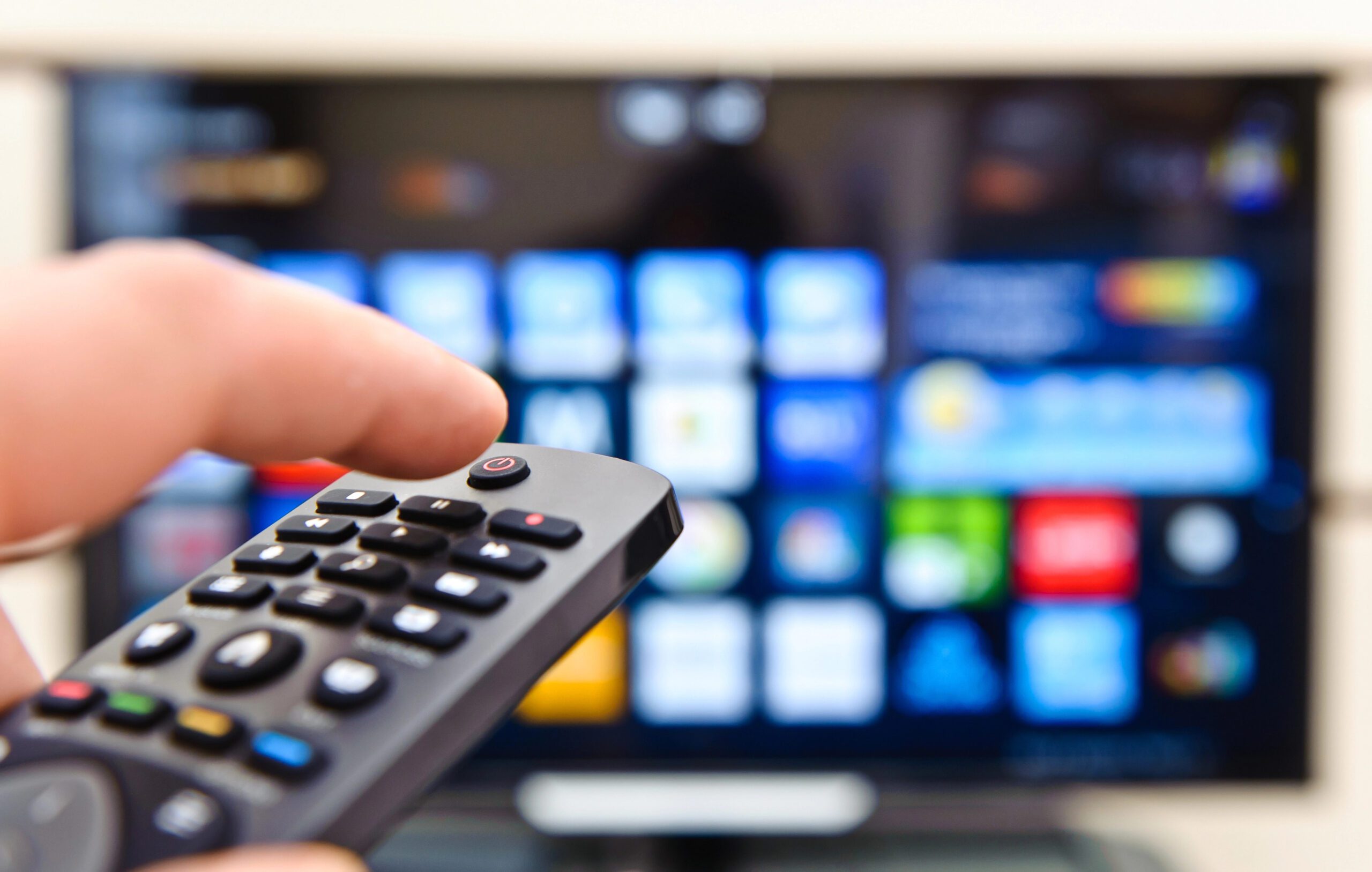 Close up of hand holding a remote pointed at a smart TV screen with many icons