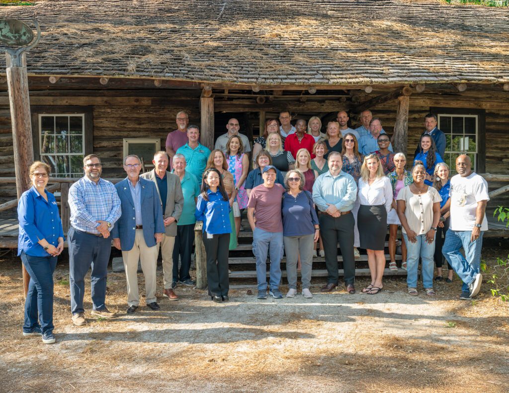 Pinellas Citizen University participants, County Commissioners, and county staff pose in front of the McMullen-Coachman Log Cabin at Heritage Village.