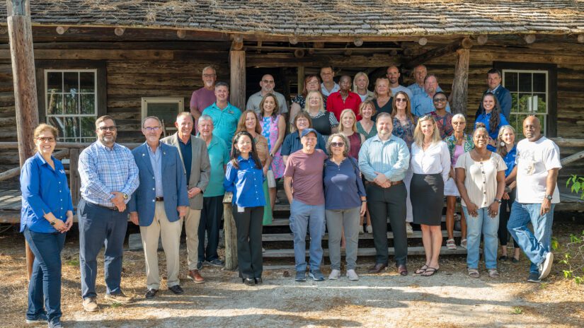 Pinellas Citizen University participants, County Commissioners, and county staff pose in front of the McMullen-Coachman Log Cabin at Heritage Village.