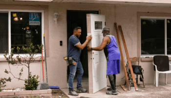 Two men work to put a new door on a home.