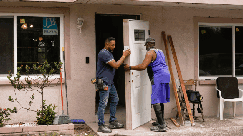 Two men work to put a new door on a home.