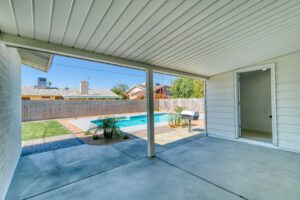 A photo of an outside patio area with nothing in it, looking into the yard with a pool with no items.