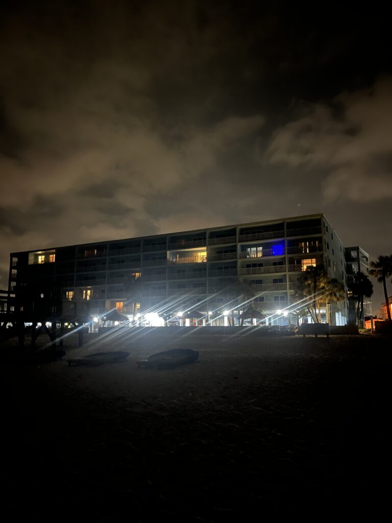 A beachfront condominium is lit up at night on Indian Shores. White lights shine brightly at the bottom of the building.