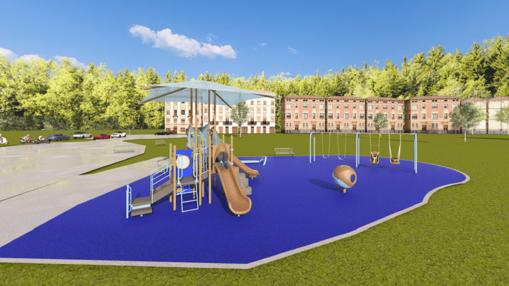 The image shows an outdoor playground set on a bright blue rubberized safety surface with an irregular rounded shape. In the foreground, a large play structure features multiple ramps, railings, and platforms. The structure includes two brown slides—one straight and one curved—plus a small set of stairs, activity panels, and a large square shade canopy supported by tall posts. To the right of the main structure, there is a swing set with several swings, including two bucket‑style swings and two standard belt swings. Near the swing set is a small, spherical, mounted play element with circular openings.
Around the play area, two green metal benches face the playground. To the left, a wide paved walkway curves around the edge of the scene and appears to lead toward a parking area where several vehicles are parked. In the background, a row of multi‑story brick buildings stands in front of a dense treeline of tall green trees. The sky is bright blue with scattered clouds, and the lighting indicates a clear, sunny day.