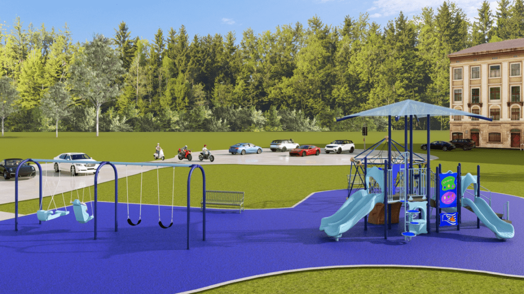 The image shows an outdoor playground built on a bright blue rubberized safety surface with a curved, irregular edge. The playground is located in a large grassy area bordered by a dense forest of tall green trees. A paved road appears behind the playground, where several vehicles, including cars and motorcycles, are traveling or parked. On the far right, part of a multi‑story brick building is visible.
In the foreground on the left, a swing set with a blue metal frame includes two adaptive molded-seat swings and two standard belt swings. A green metal bench is positioned behind the swing set, facing the play area.
To the right of the swing set, the main play structure features multiple elevated platforms connected by railings, steps, and ramps. A large roof canopy supported by tall posts provides shade over the central portion of the structure. Several light‑blue slides extend outward from the structure, including a straight slide and a gently curved slide. Activity panels with bright colors and simple graphics are mounted along the lower sections of the structure.
Behind the main play structure, partially visible, is a large rope‑climbing dome made of blue and black interconnected ropes attached to a metal frame.
The sky is bright blue with a few small clouds, suggesting clear weather and strong sunlight.