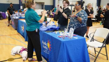 Pinellas County staff at an information table speak with an attendee using American Sign Language at a previous Pinellas County Deaf Fest event. Other information tables and attendees can be seen in the background.