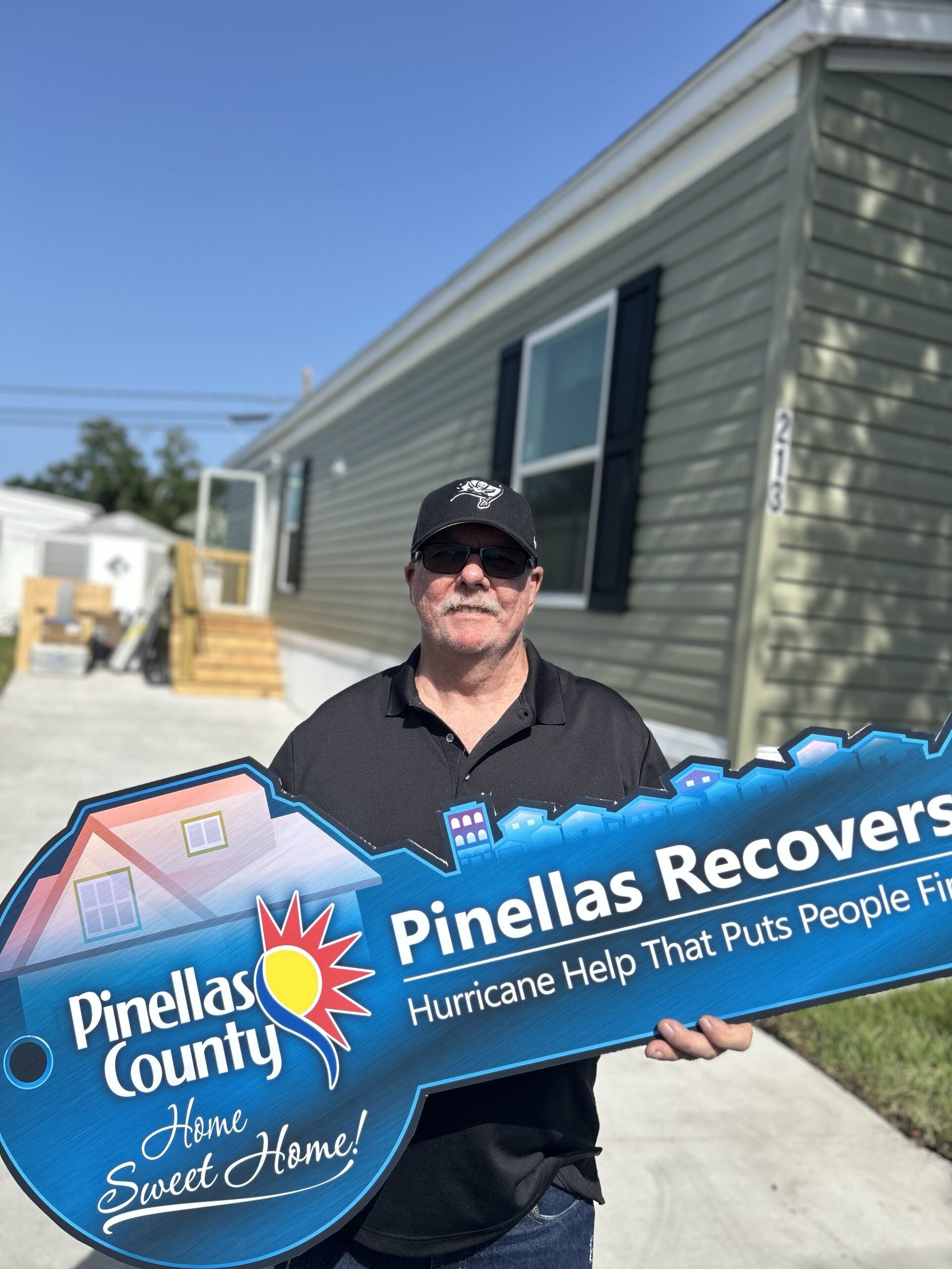 Richard Brill holds up an oversized sign shaped as a key to commemorate his mobile home having been completely replaced by the Pinellas Recovers program.
