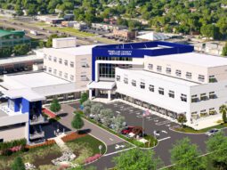 A rendering of the North County Service Center being built 2026-2028. the building is L shaped with three levels and a parking garage on the west side.